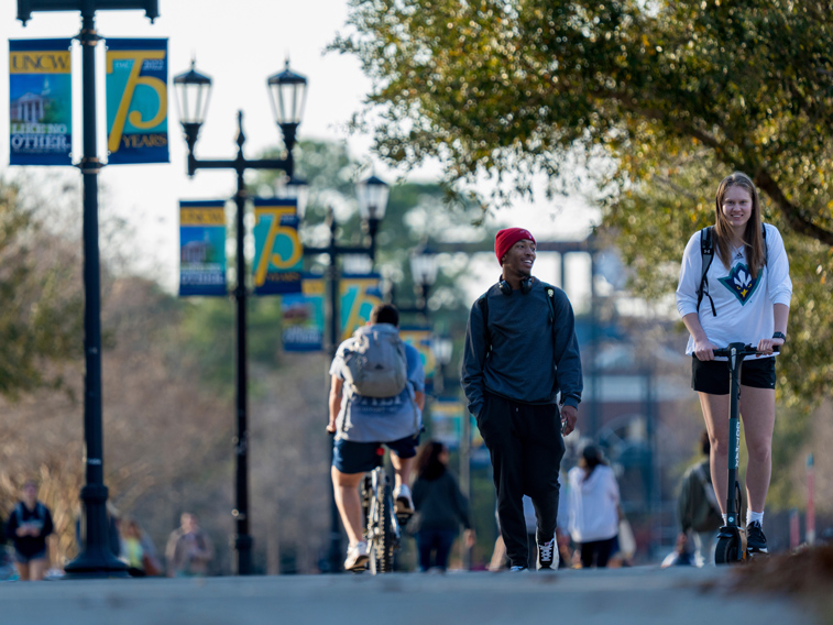 Students walking and riding scooters on a UNCW street