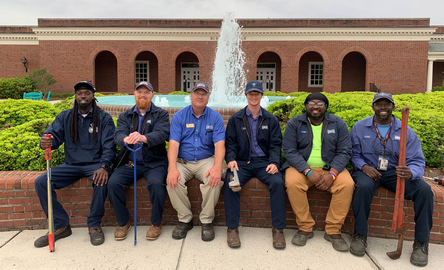 UNCW plumber team sitting in front of a fountain on campus