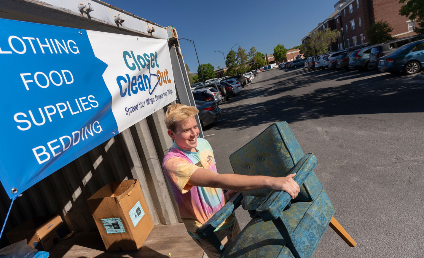 Male presenting student lifts a teal chair out of a donation container