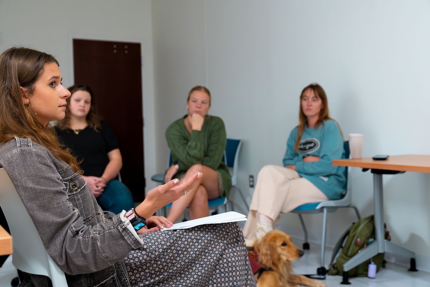 four master of social work students sit together to practice their skills while a golden retriever service dog lies on the floor.