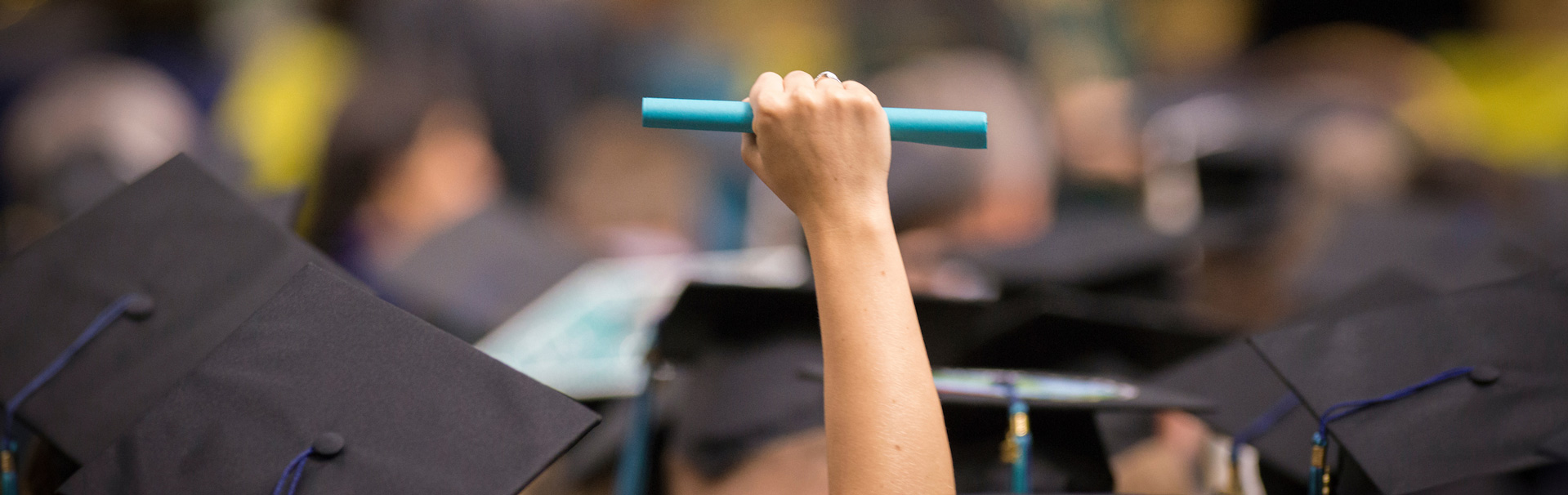 A student holds their degree in their fist above all the graduation caps of their peers at commencement.