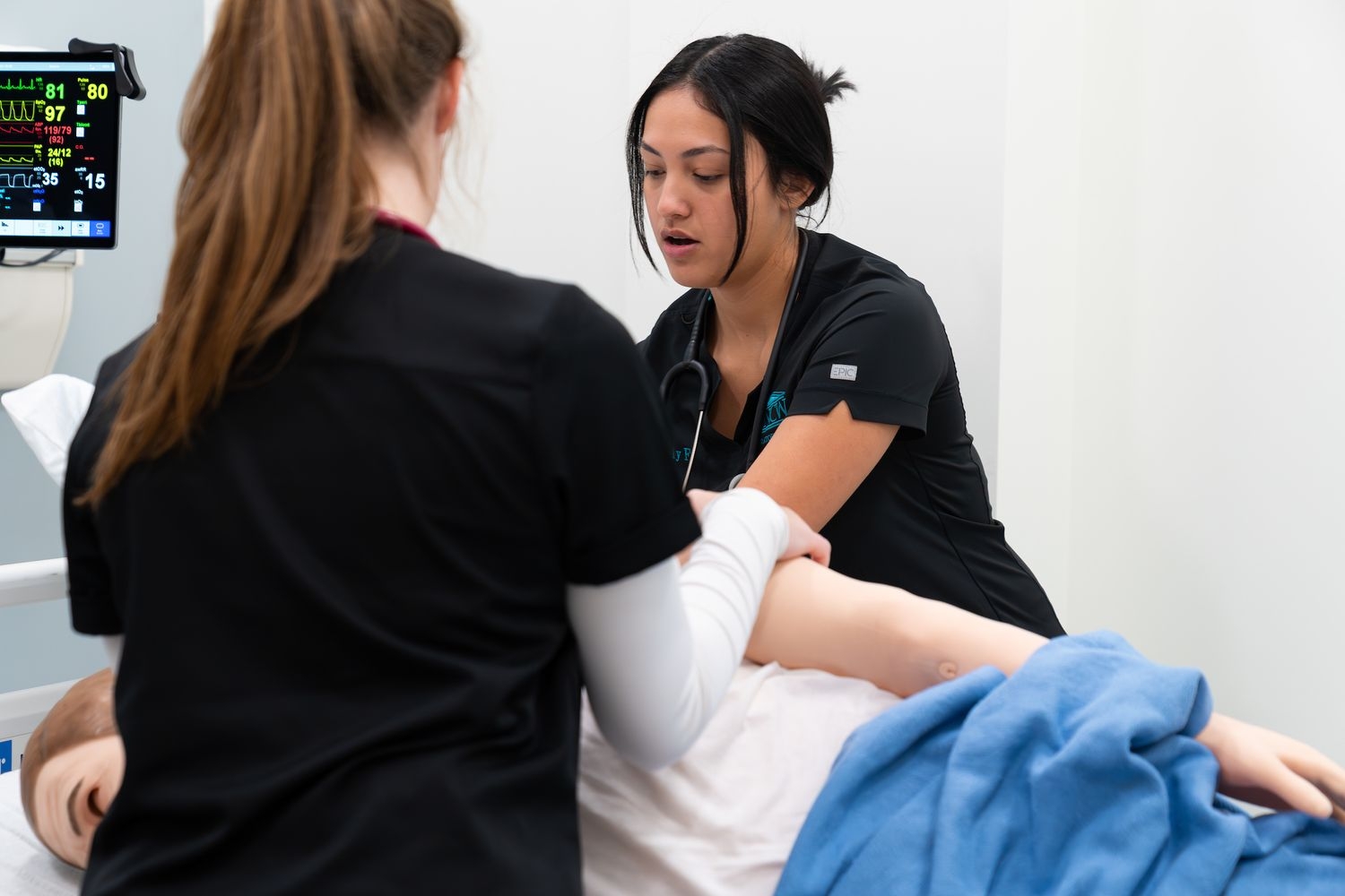 Two respiratory therapy students shift a manikin onto it's side to practice percussion.