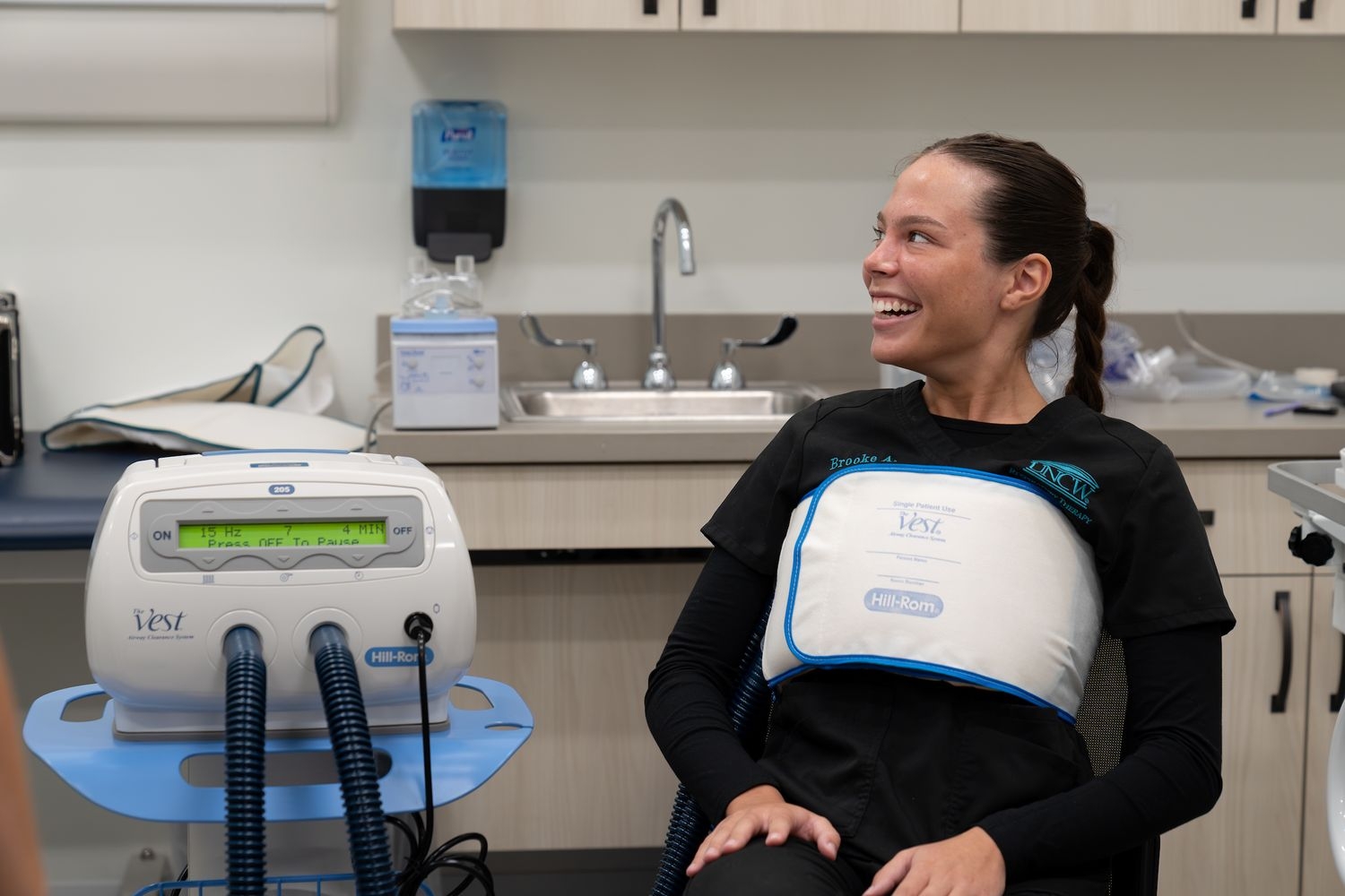 A respiratory therapy student wearing a vest, a vibrating tool used to clear chest congestion.