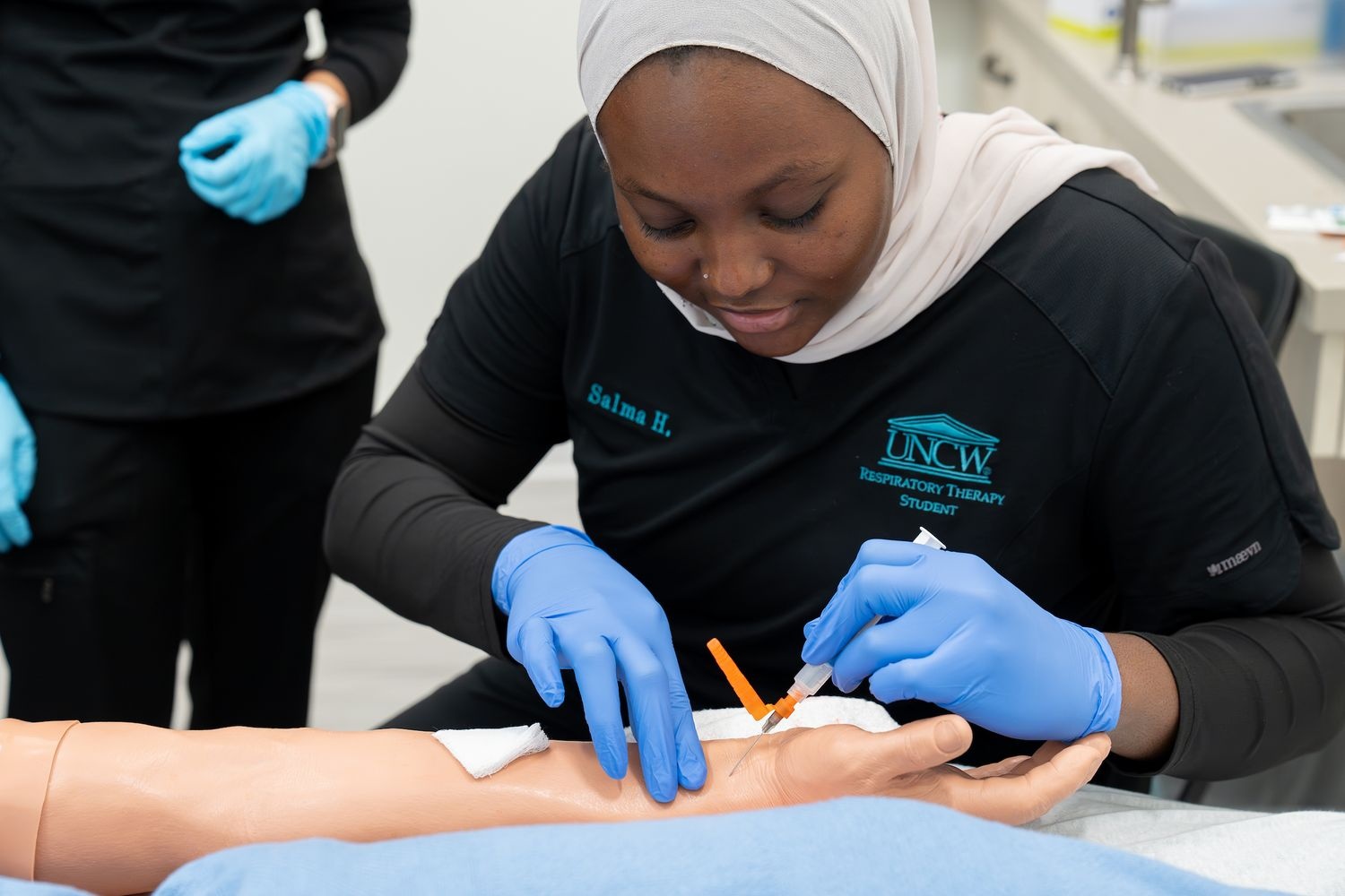 A respiratory therapy student practices drawing blood from the radial artery of a manikin. 