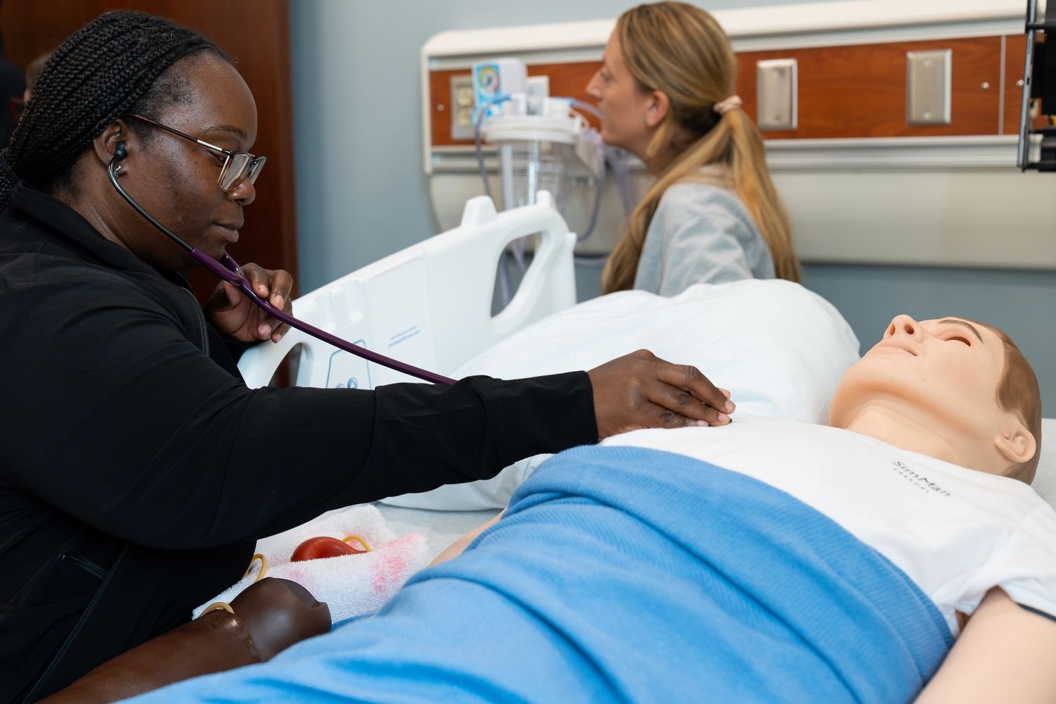 A respiratory therapy student listens to the lungs of a manikin using a stethoscope.