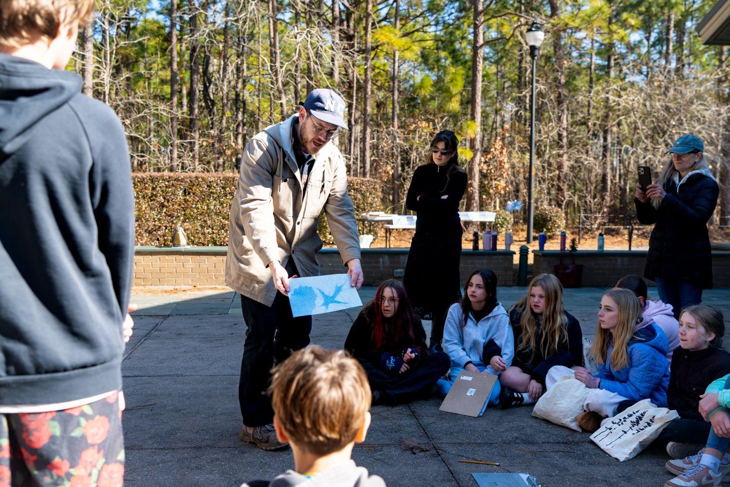 James Farley shows seated children cyanotypes of longleaf pine trees outside the Cameron Art Museum