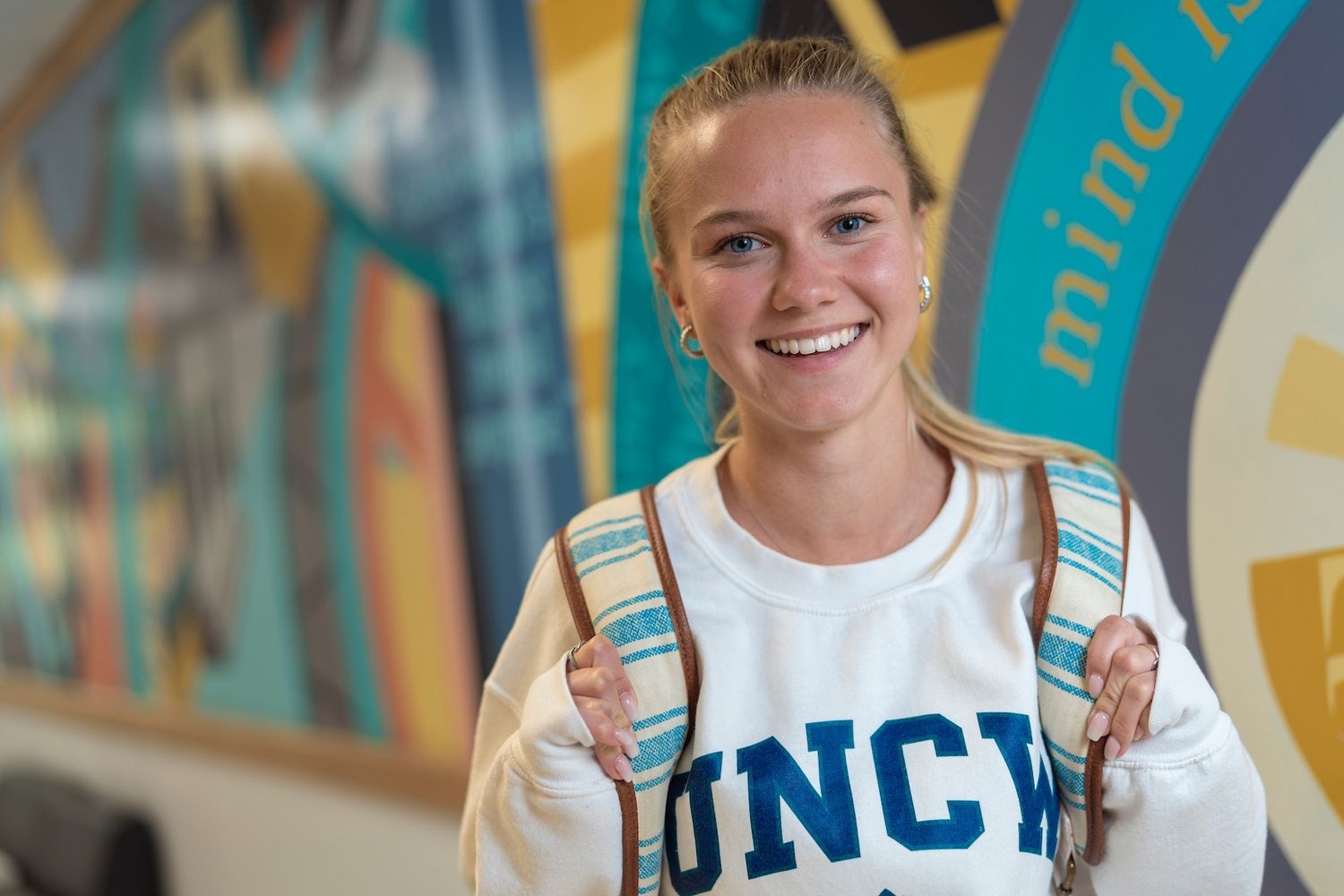female student in UNCW sweatshirt smiling in hallway