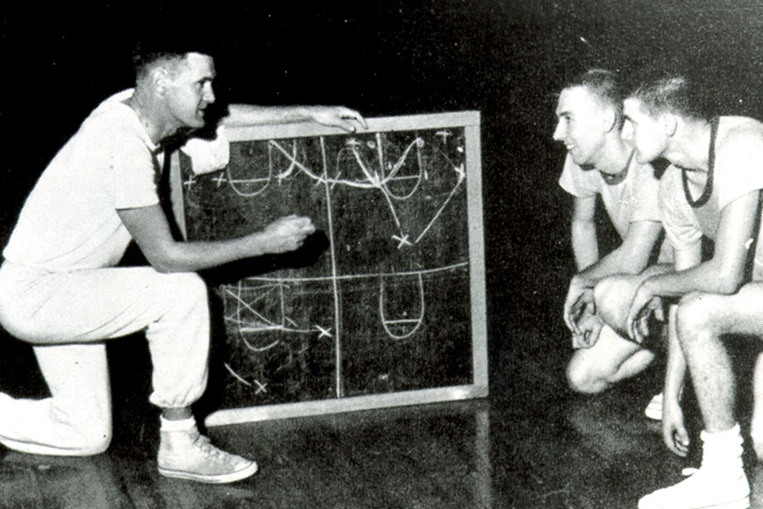 Coach outlines plays on a board for two basketball players