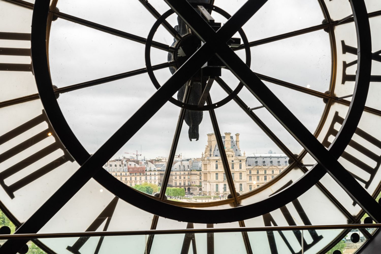 View of the louvre through a large clock from museum d'orsay in Paris