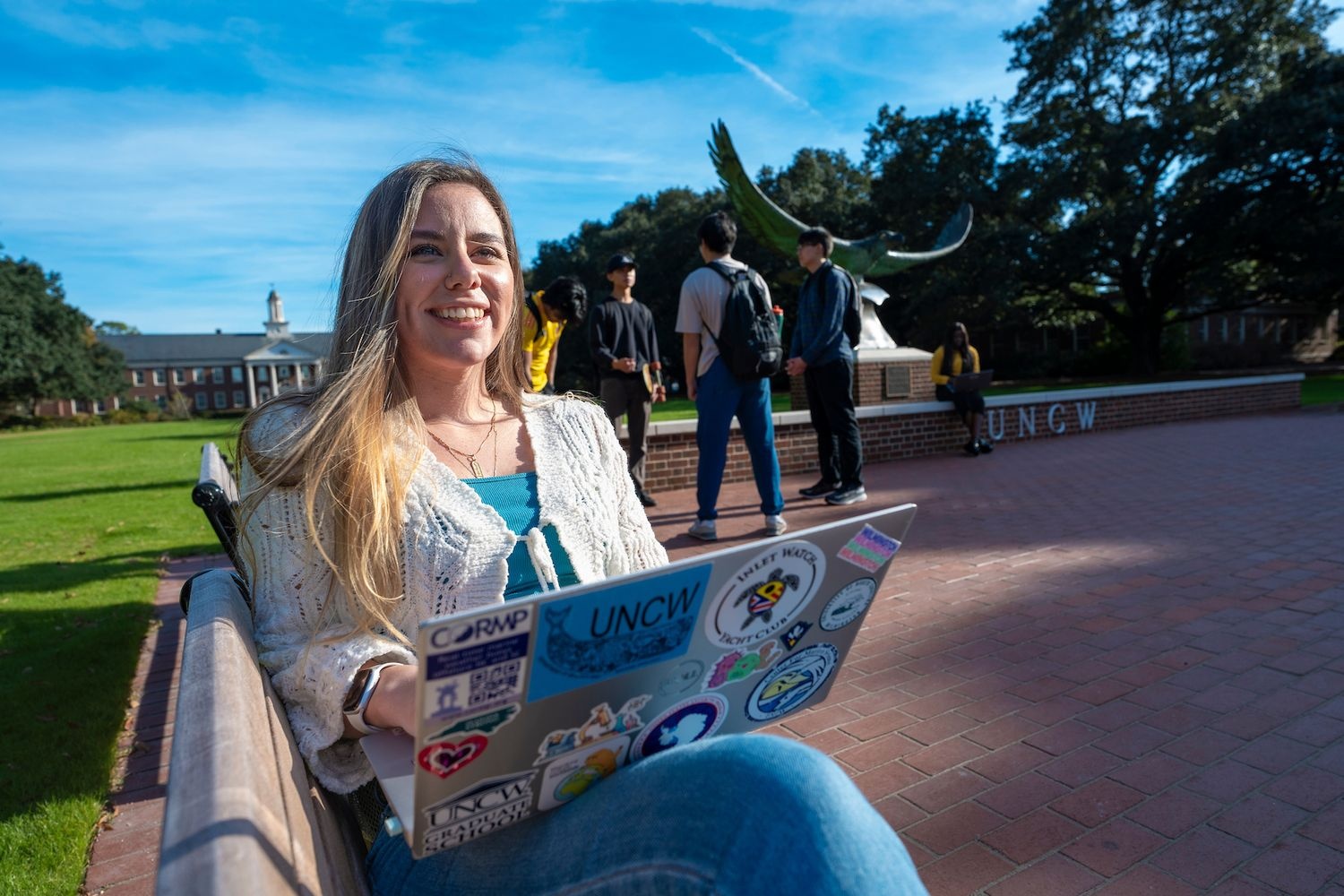 Woman sits on bench with soaring seahawk statue in background and open laptop on her lap