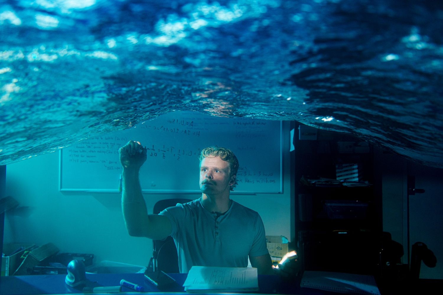 Looking through the glass and water of the wave flume, a researcher on the opposite side writes on the glass of the tank while the tank produces waves.