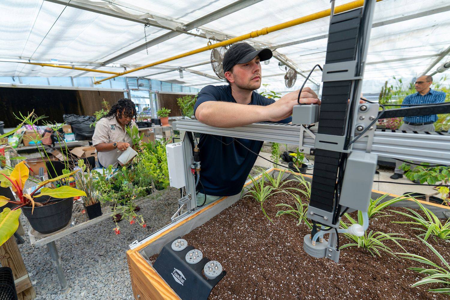 Student in the Intelligent Systems Engineering program (ISE) making adjustments on a machine in the greenhouse