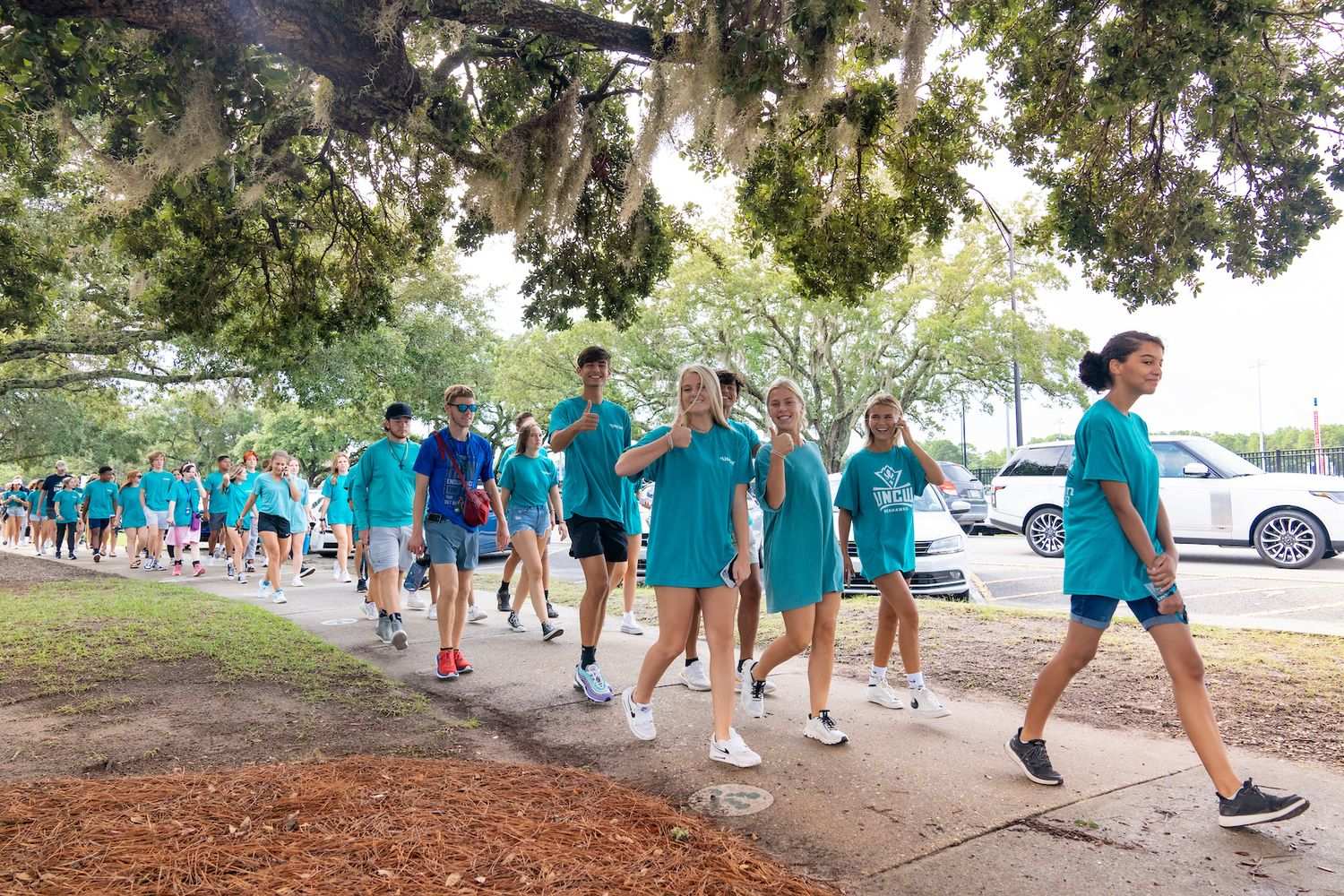 Students walking to Trask Coliseum wearing teal, giving a thumbs up