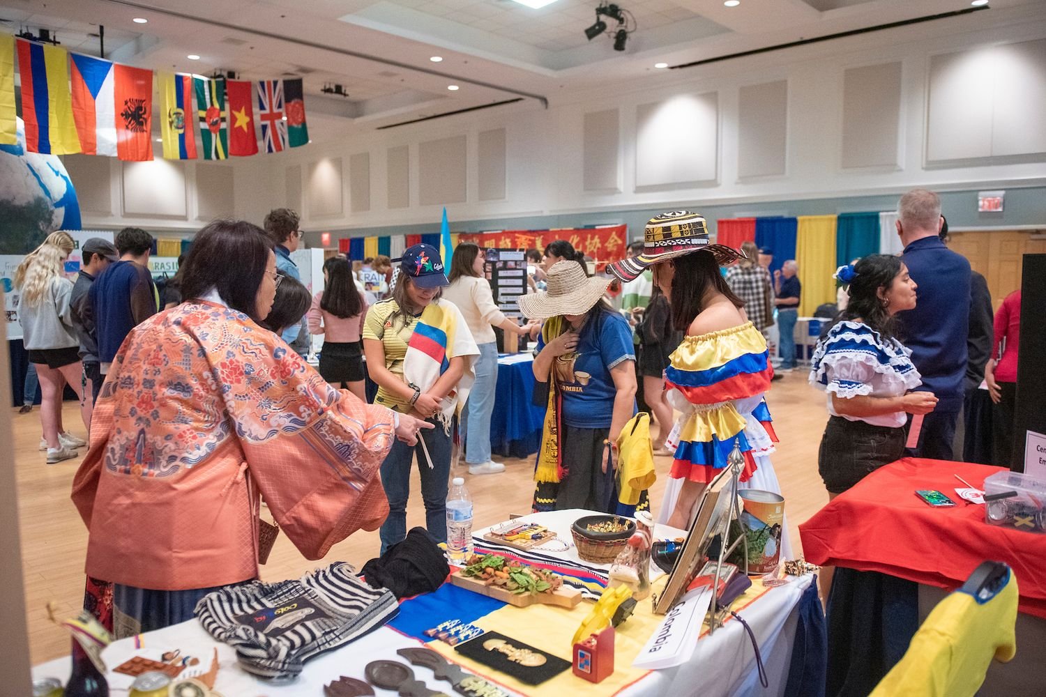 A bustling cultural fair showcasing diverse nationalities and traditional outfits, including the Colombian colors of yellow, blue, and red prominently featured in dresses and hats.