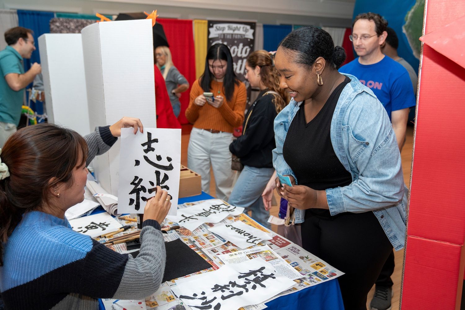 A woman does calligraphy at an event on the campus of UNC Wilmington, while other people watch.