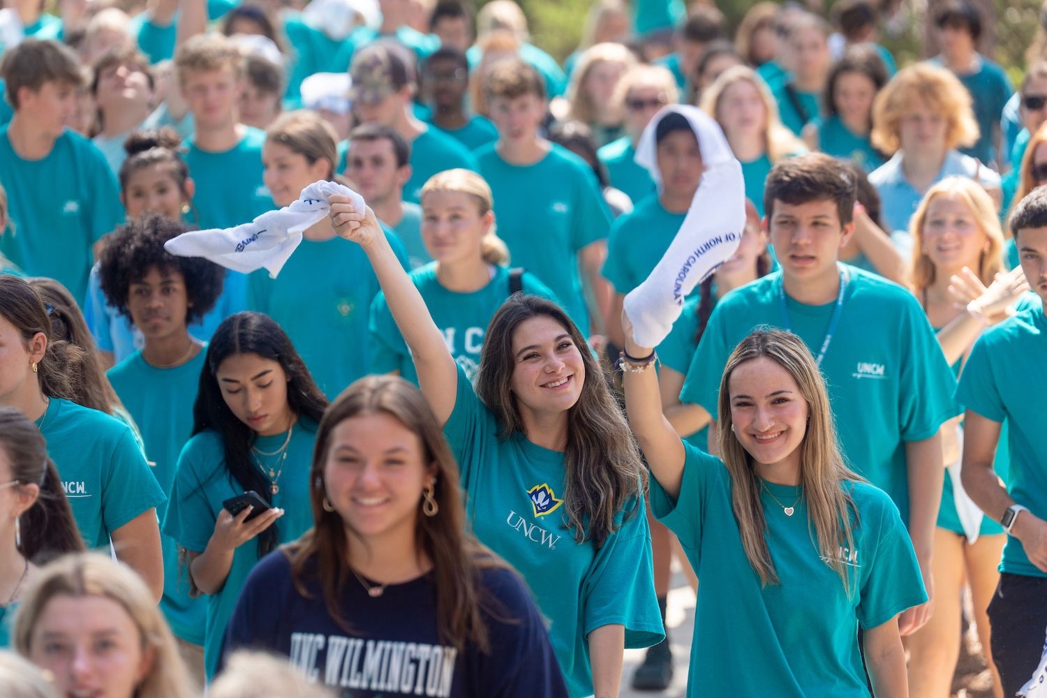 Students in crowd wearing teal and twirling towel
