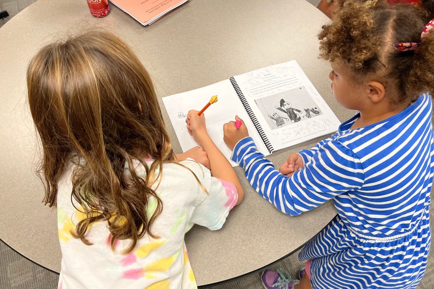 Two children writing in a pamphlet