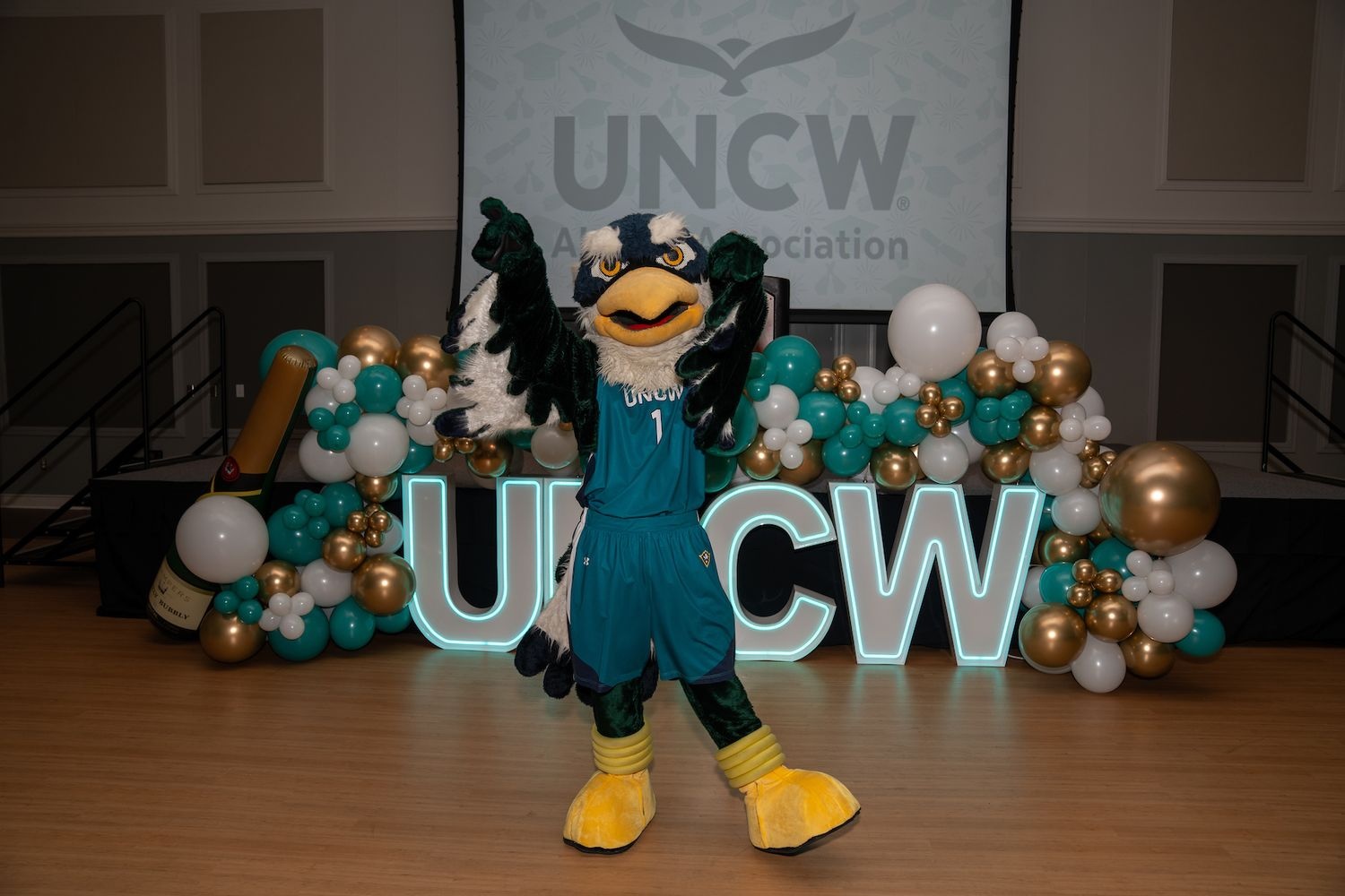 Sammy Seahawk posing in front of UNCW sign on basketball court