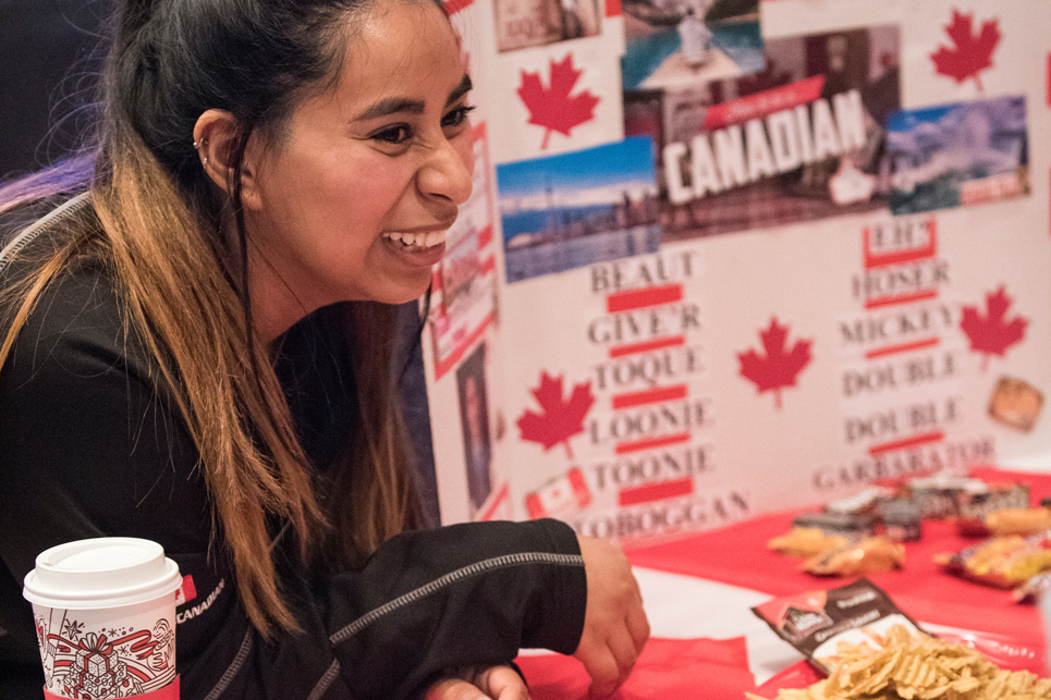 Student at an iFest exhibit smiles in front of a Canada poster board.