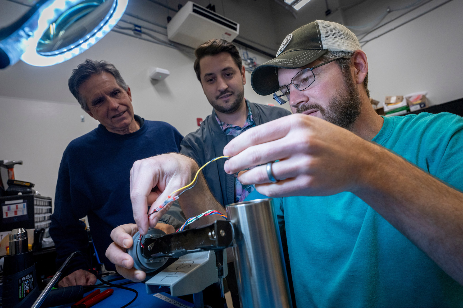 Student Dayton Thompson assembles sensors developed by Dr. Ryan Mieras (C), assistant professor of coastal engineering. Sean Griffin (L) of Proteus Technologies is working with Mieras to help build the sensors that will be used to measure sand movement in the swash zone.