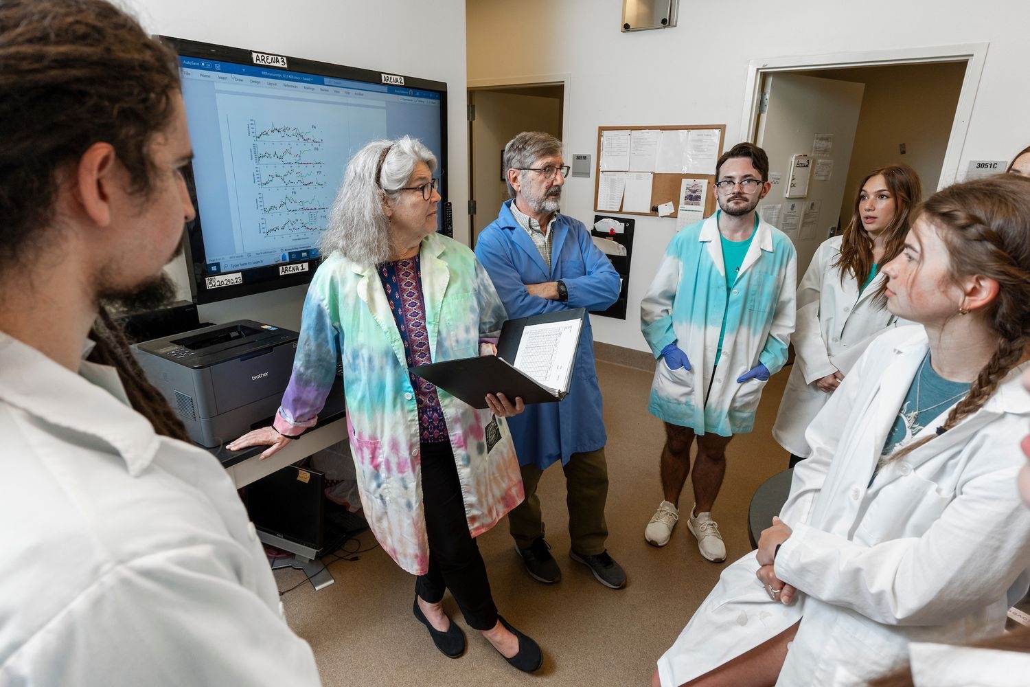 UNCW faculty and students in lab coats gather to discuss their work