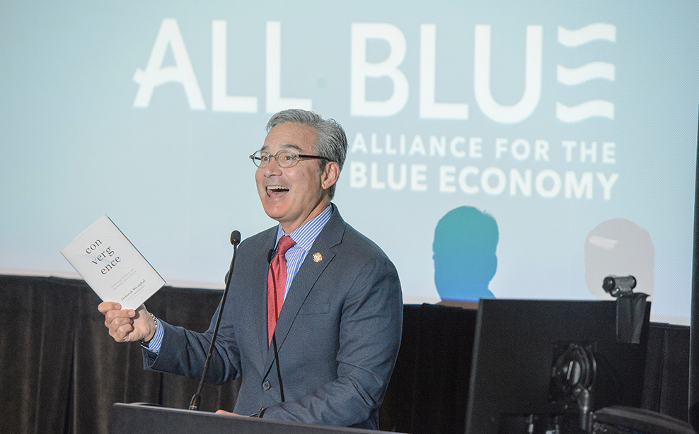 Speaker at an All Blue event stands on stage during a presentation