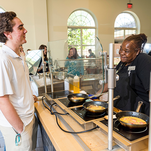 A student in front of an omelet station talking to the server