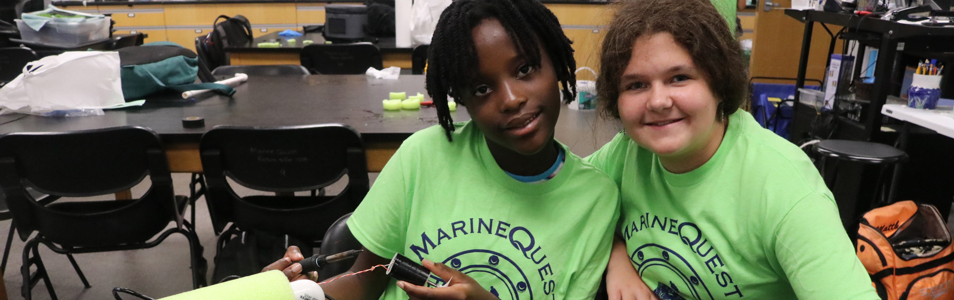 2 students in green marinquest shirts smile for the camera
