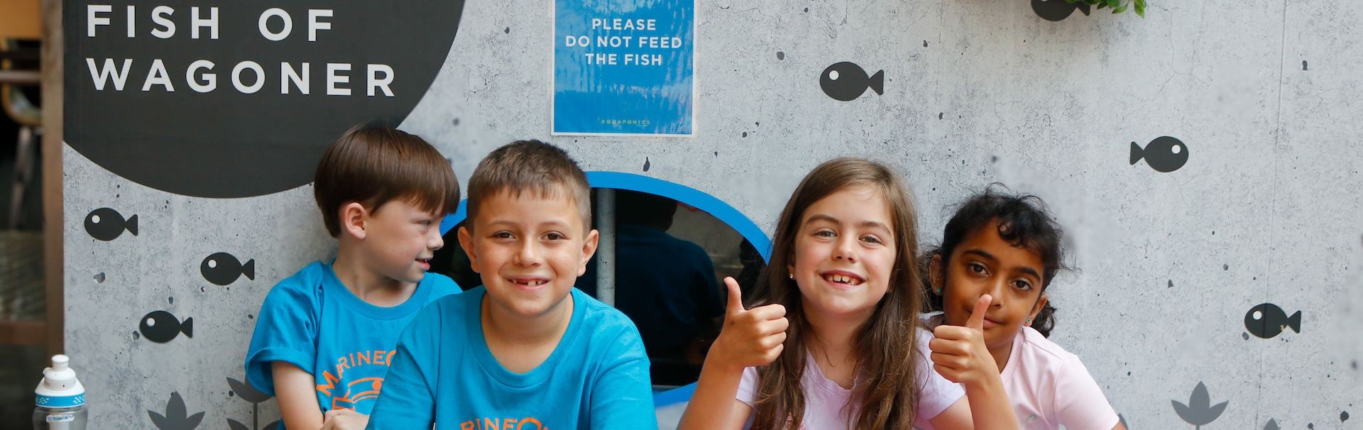 Junior Aquaculturist campers sitting in front of display with thumbs up