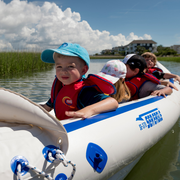 A group of small children in an inflatable sea kayak on a marshy body of water