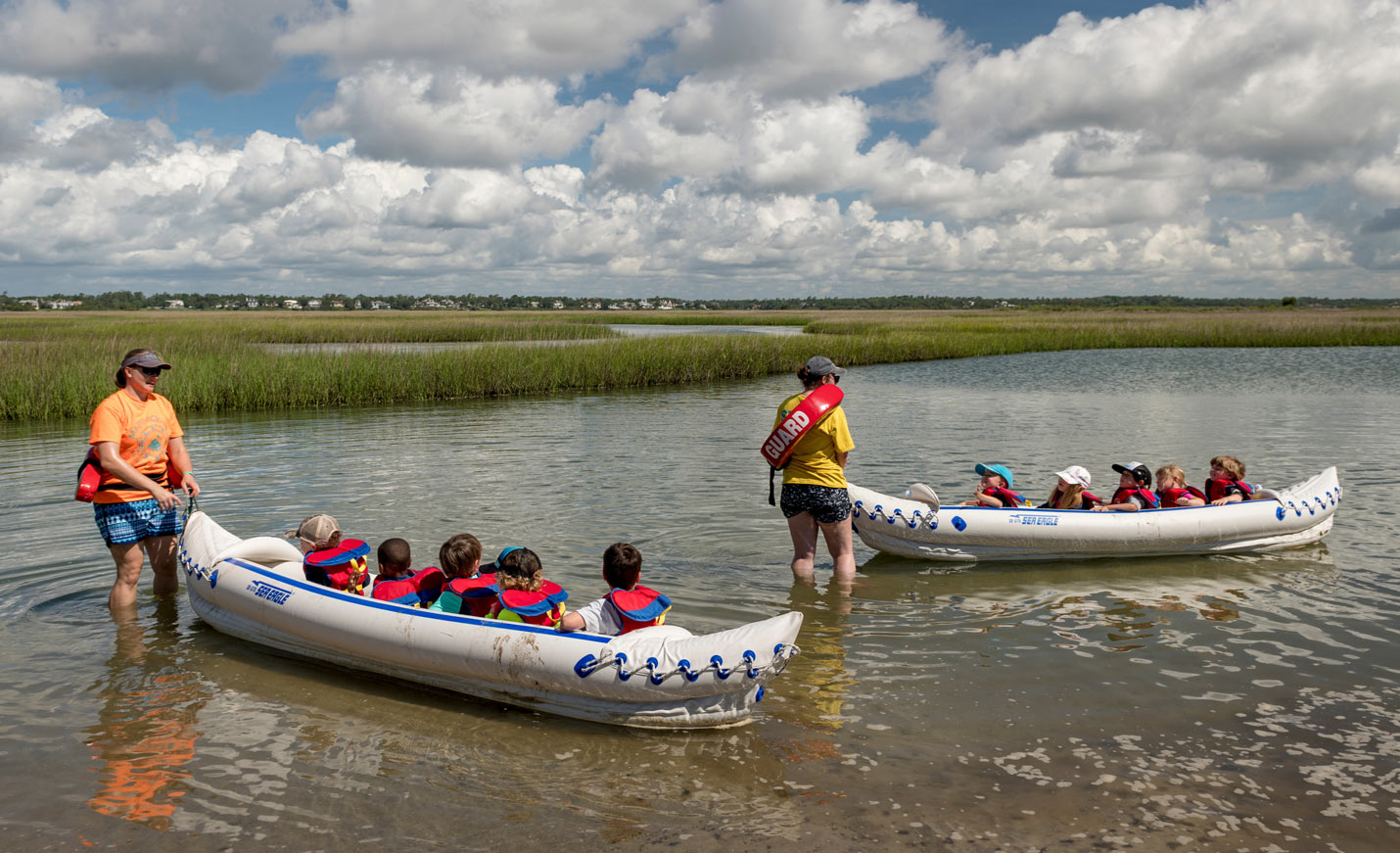 Two staff carrying youth in inflatable kayaks