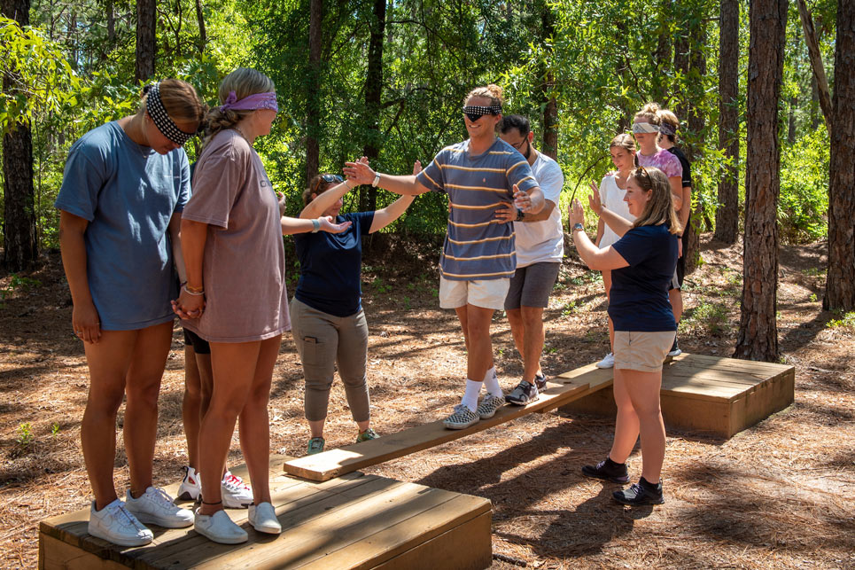 Students are pictured engaging in a low ropes balancing activity on the Challenge Course